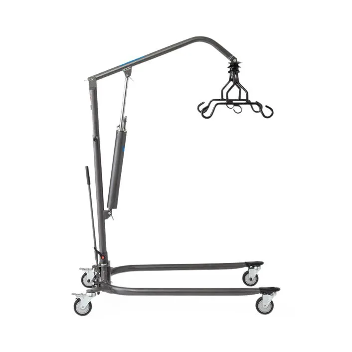 A grey steel patient lift on a U-shaped base with four casters, an angled boom with a hydraulic cylinder and a long pump handle, and a black spreader bar with hooks hanging from the end of the boom